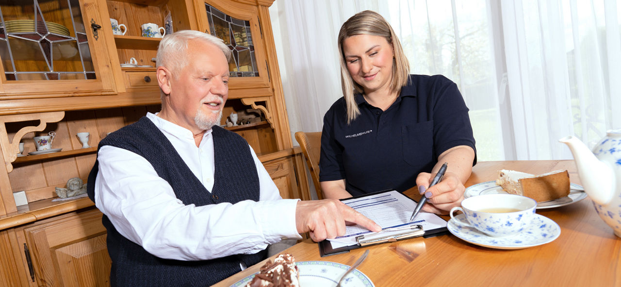 Pflegeberaterin mit älterem Herrn an einem Tisch