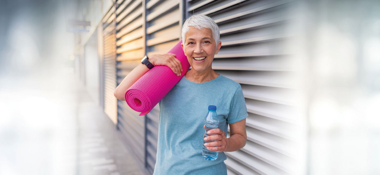 Eine ältere Frau mit Yogamatte auf dem Arm