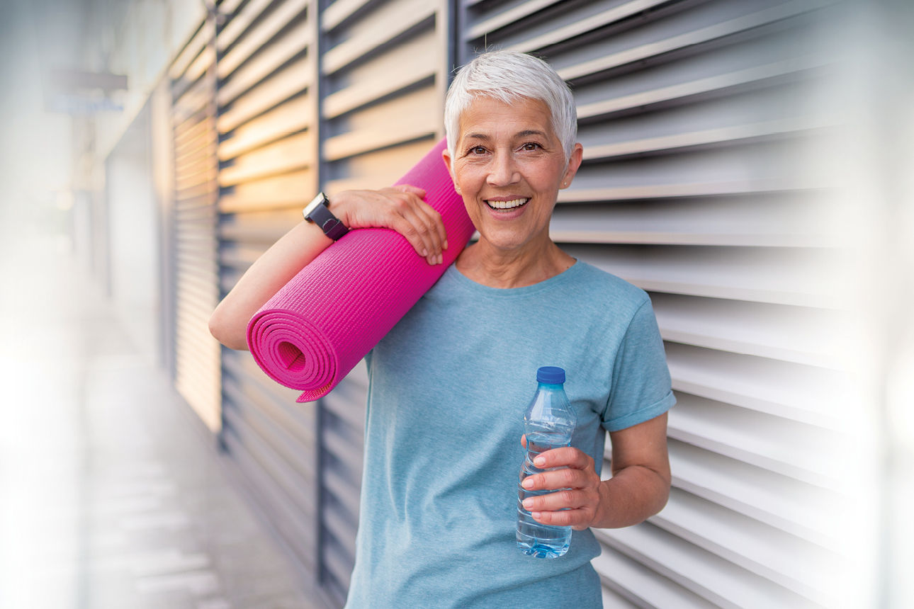 Eine ältere Frau mit Yogamatte auf dem Arm