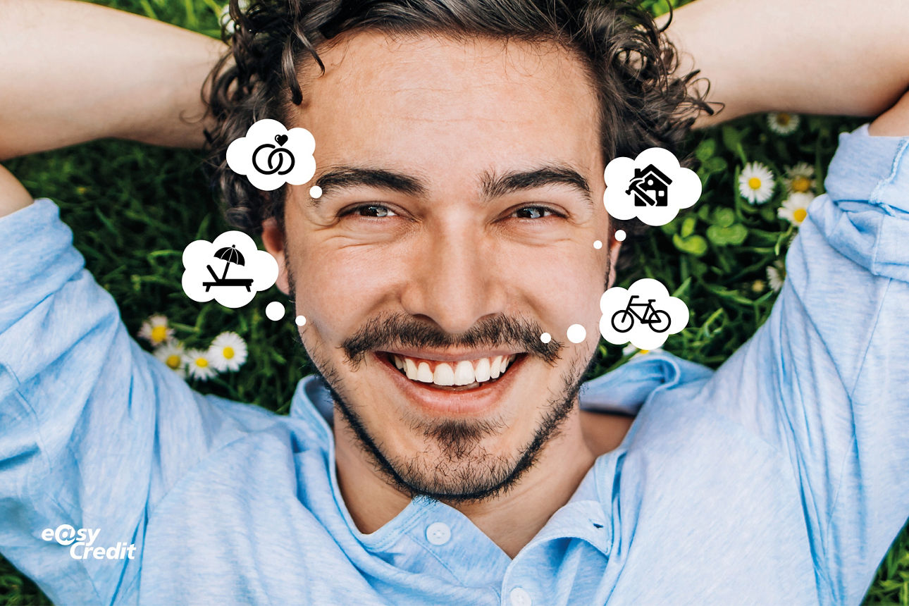 Mann liegt auf dem Rücken im Gras und lächelt in die Kamera