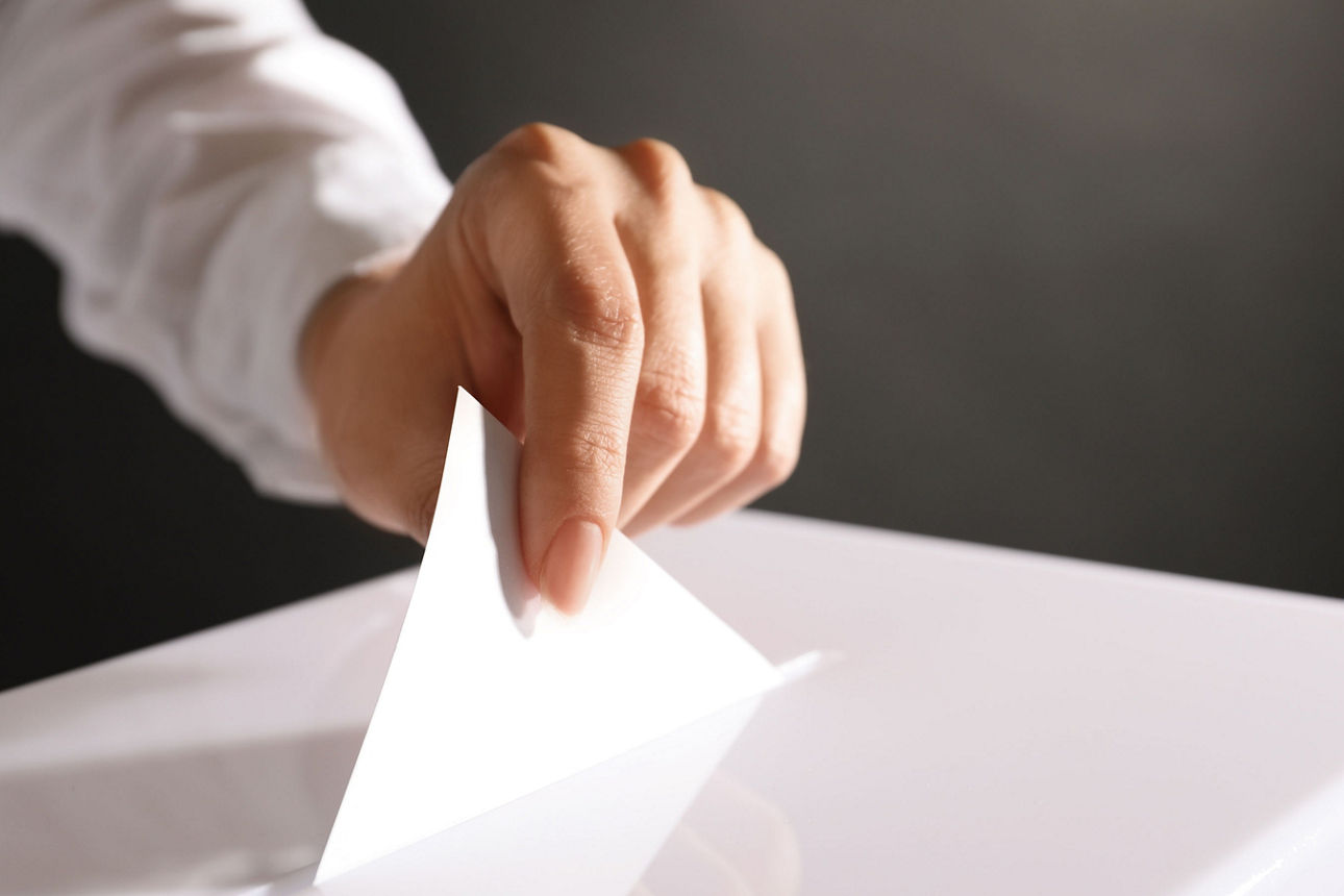 Hand steckt ein Blatt in eine weiße Wahlbox