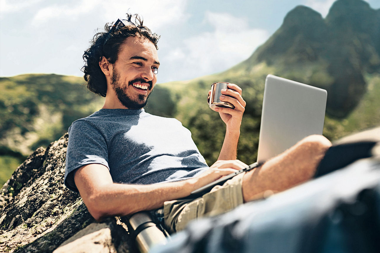 Mann sitzt in den Bergen am Laptop