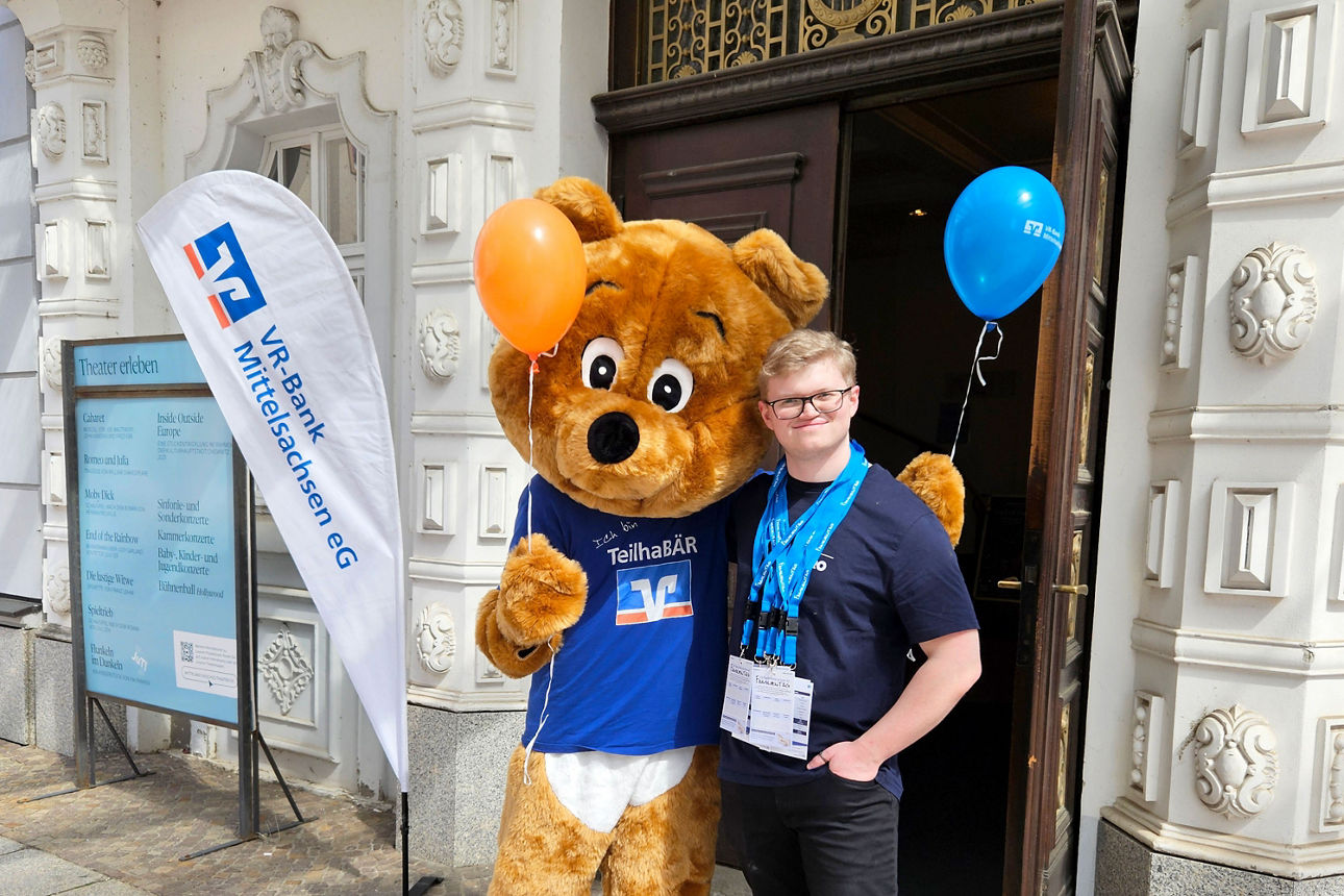 Maskottchen der VR-Bank Mittelsachsen und ein Mitarbeiter vor dem Eingang des Theaters