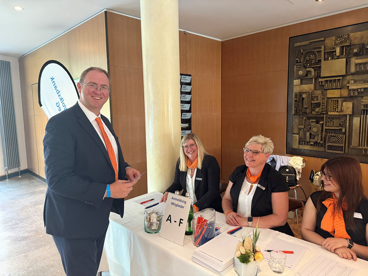 Ein Mann im Anzug spricht an einem Empfangstisch mit drei Frauen, die für die Registrierung zuständig sind.