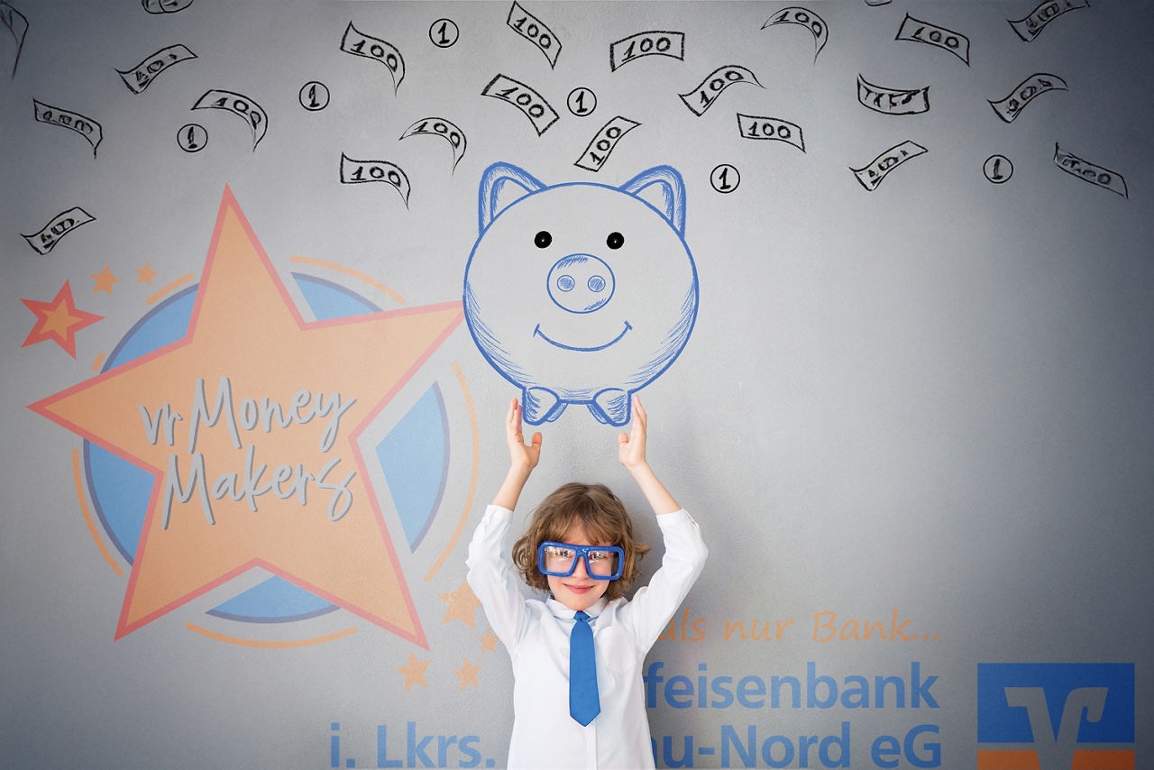 Kind hält Zeichnung eines Sparschweins vor Hintergrund mit Geldscheinen und „vrMoneyMakers!“-Schriftzug