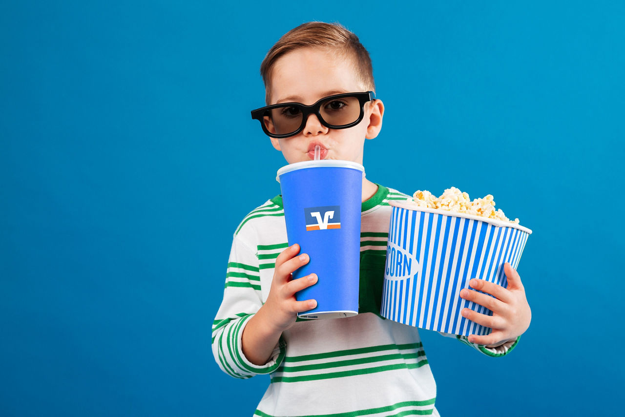 Kind mit blauem Becher und Popcorntüte vor blauem Hintergrund