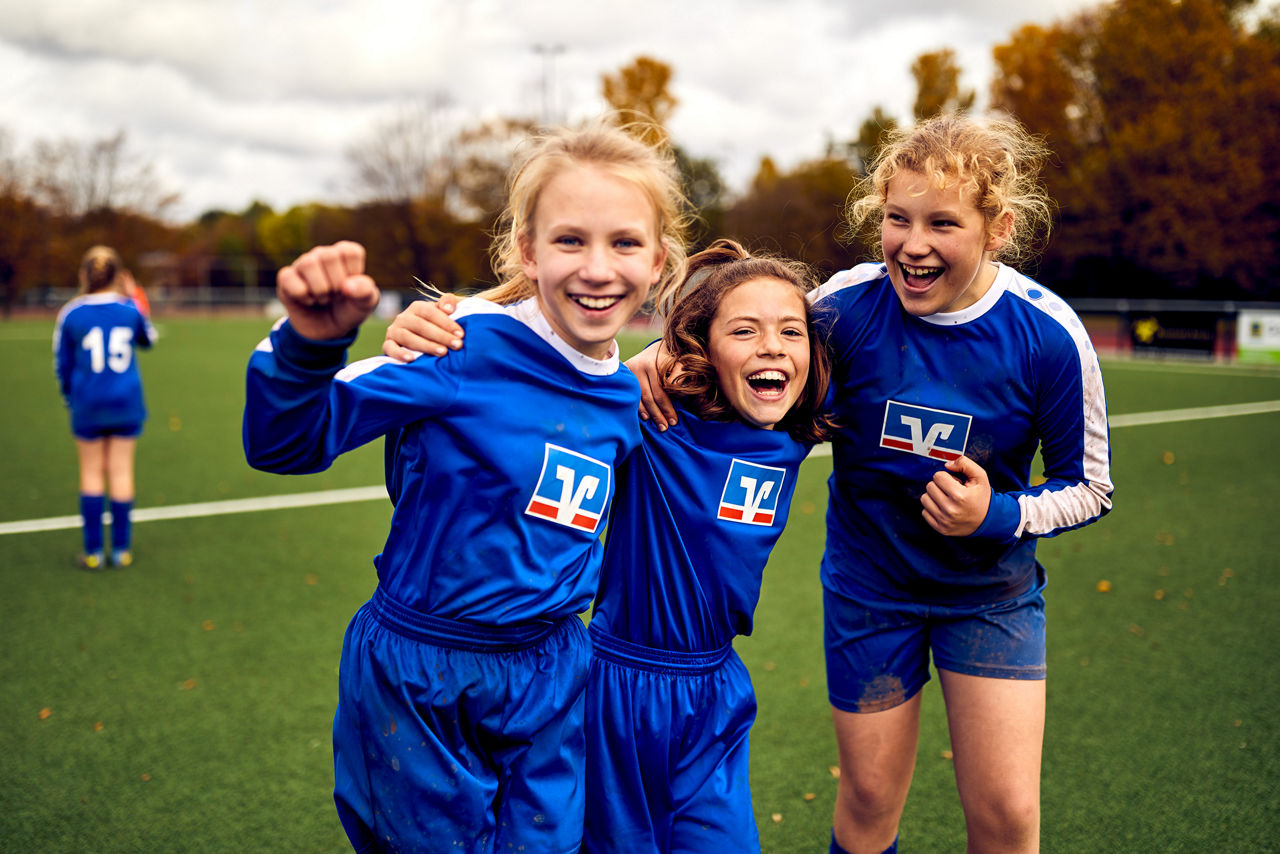 Drei Mädchen im blauen Trikot stehen am Spielfeld und jubeln