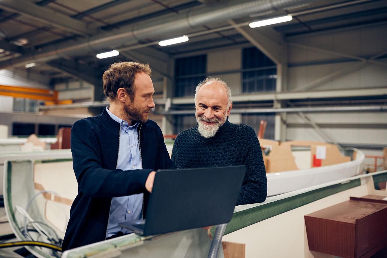 Zwei Männer stehen in einer Werktstatt vor einem Laptop