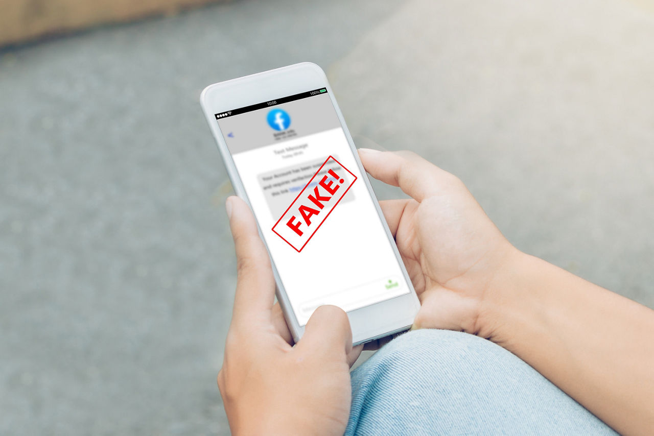Hände halten ein Smartphone mit einer Facebook-App und einem roten Stempel mit dem Text 'FAKE!' auf dem Bildschirm