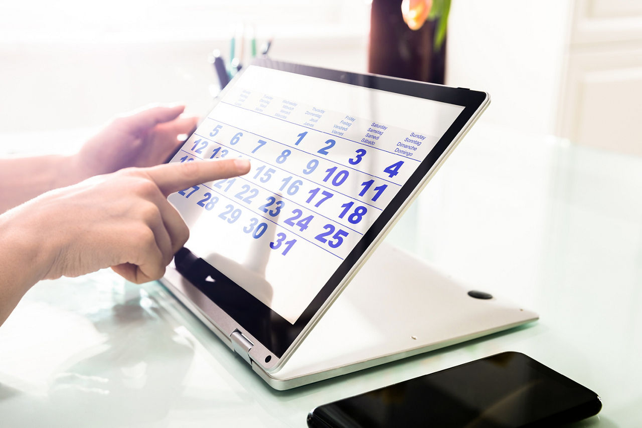 Person zeigt auf einen Kalender auf einem Laptop