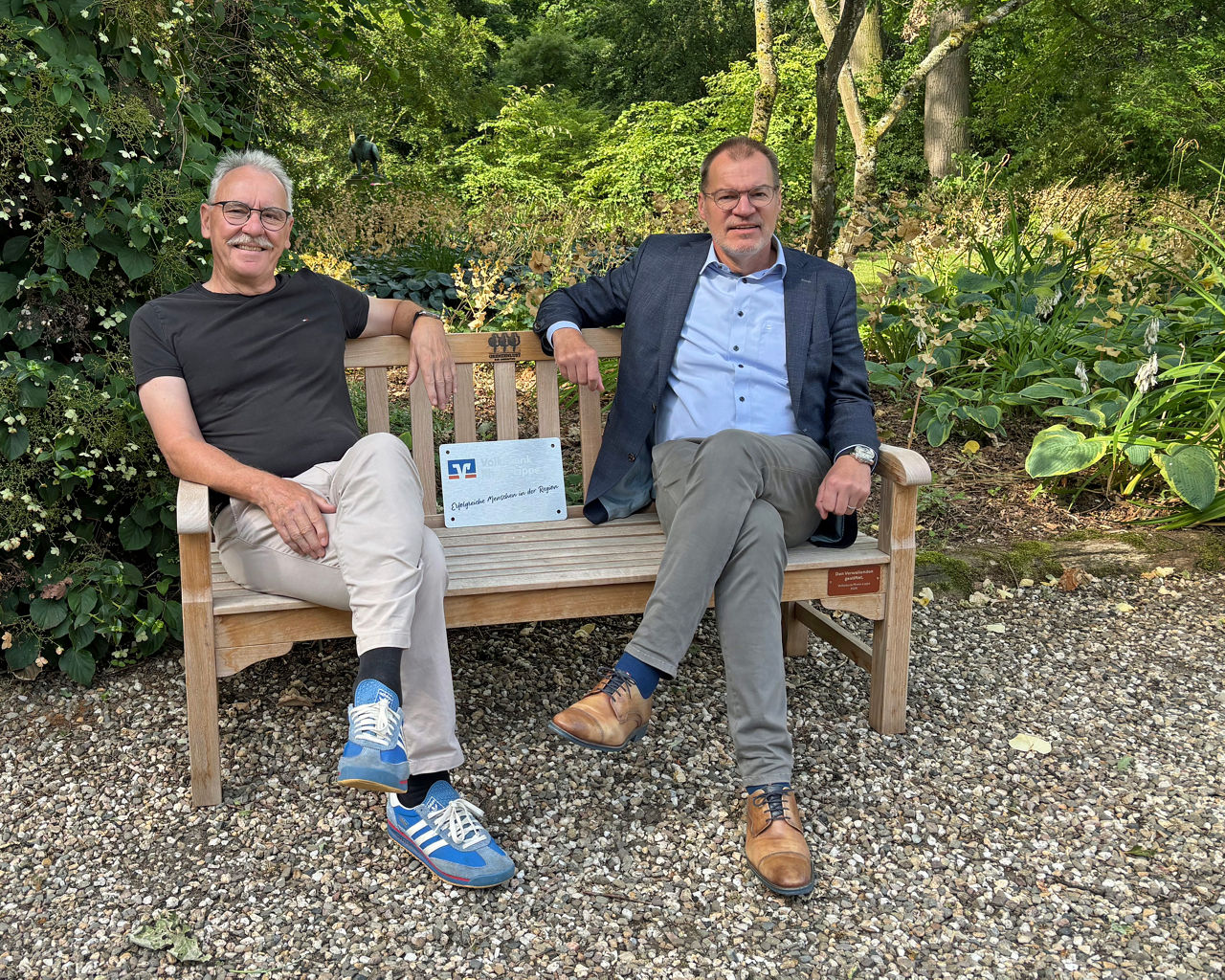 Ein Platz mit Aussicht ins Grüne: Volksbank-Vorstand Ulf Lange (rechts) und Gerd Hüsken, Vorstand der Stiftung Grenzenlust, nehmen auf der neu gestifteten Parkbank im Arboretum Grenzenlust Platz. 