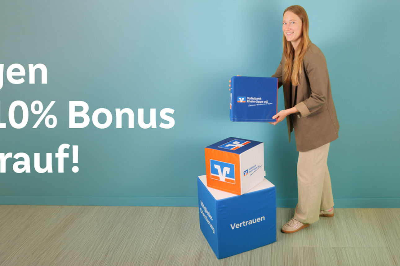 Eine Frau steht vor einer grünen Wand. Vor ihr stehen zwei große Würfel mit Volksbank-Logo drauf und sie stellt einen dritten Würfel oben drauf. Auf der Wand ist zudem der Schriftzug WIR legen bis zu 10% Bonus oben drauf.