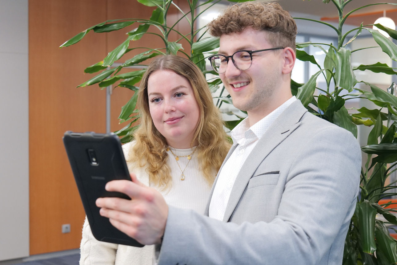 Eine junge Frau und eine junger Mann schauen zusammen auf ein Tablet und lächeln