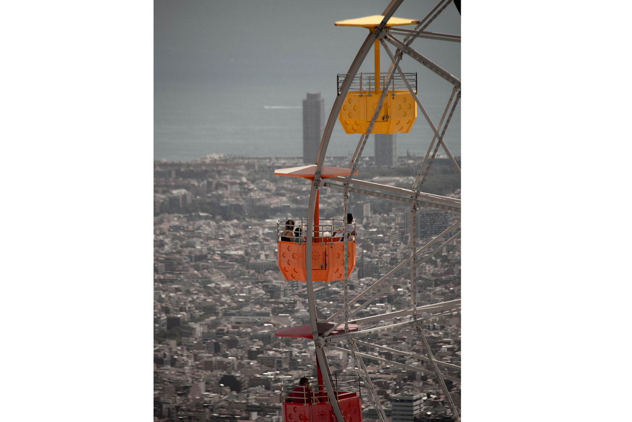 Nahaufnahme eines Riesenrads mit bunten Gondeln vor einer weitläufigen Stadtlandschaft und einem hohen Gebäude im Hintergrund.
