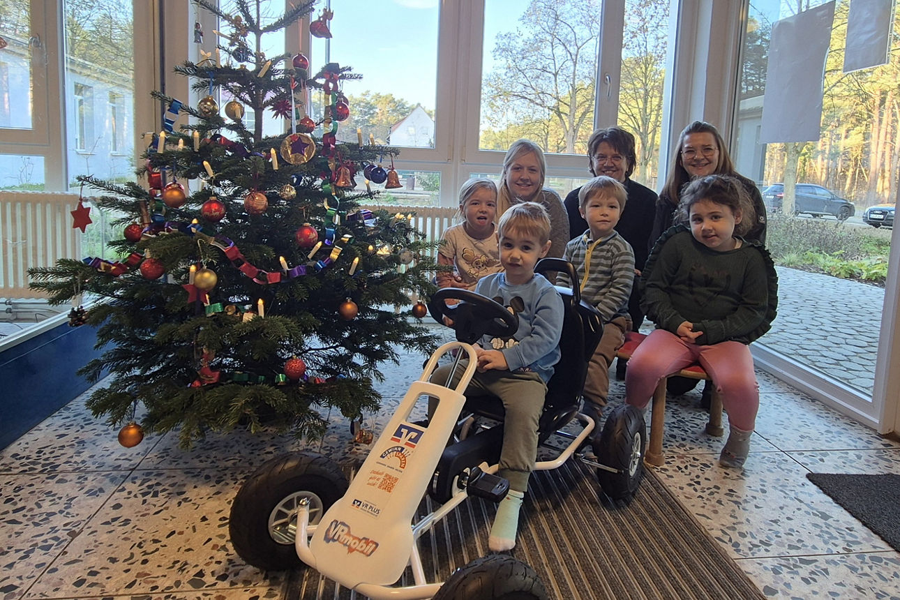 Gruppe von drei Erwachsenen und vier Kindern sitzen am Weihnachtsbaum mit einem Gokart.
