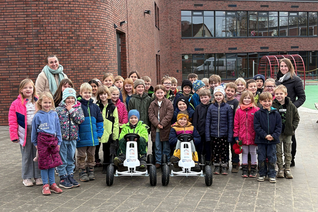 Gruppenbild einer Grundschulkinder-Gruppe mit 2 Erwachsenen und 2 Gokarts.