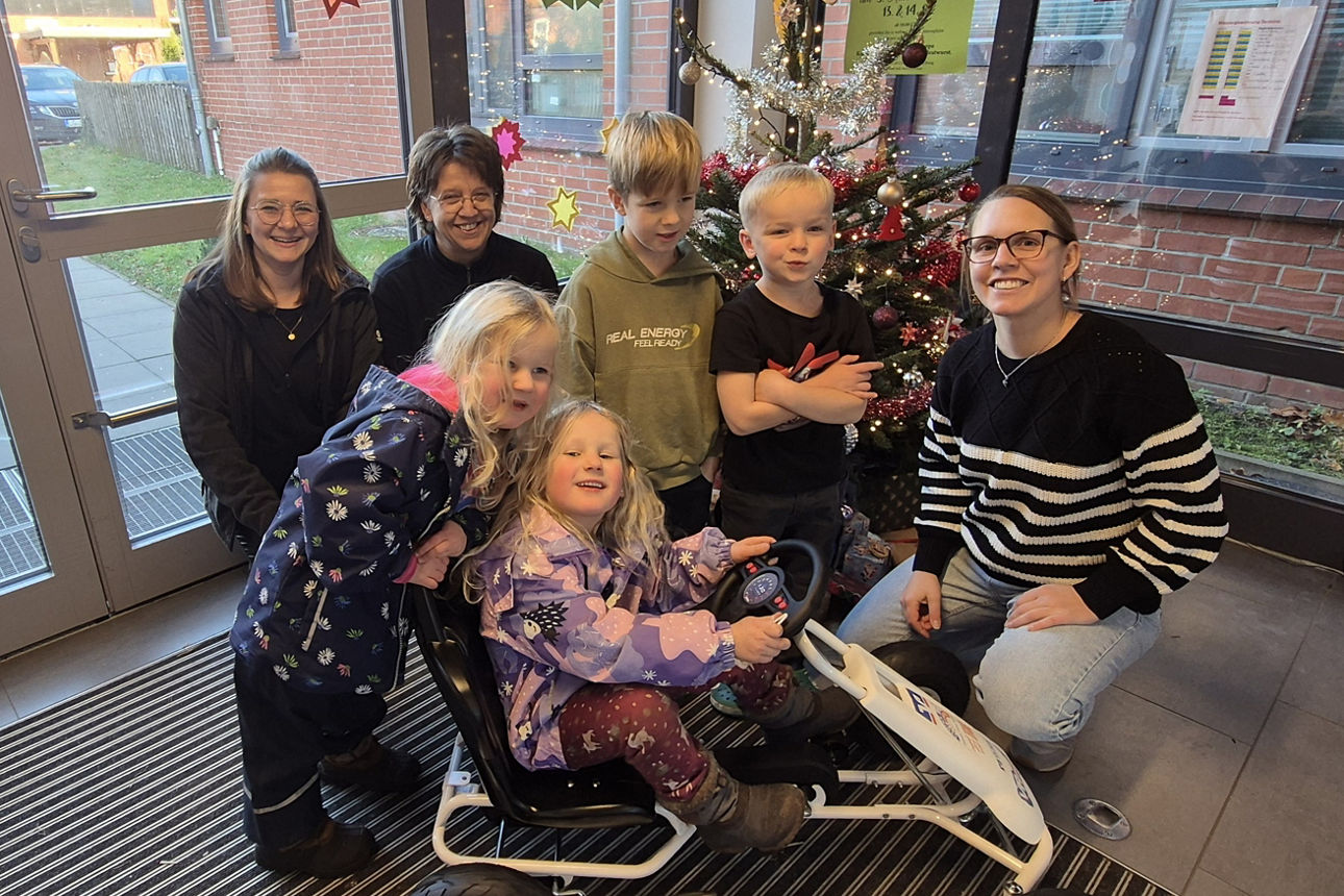 Kinder und Erzieherinnen stehen um einen Gokart und freuen sich.