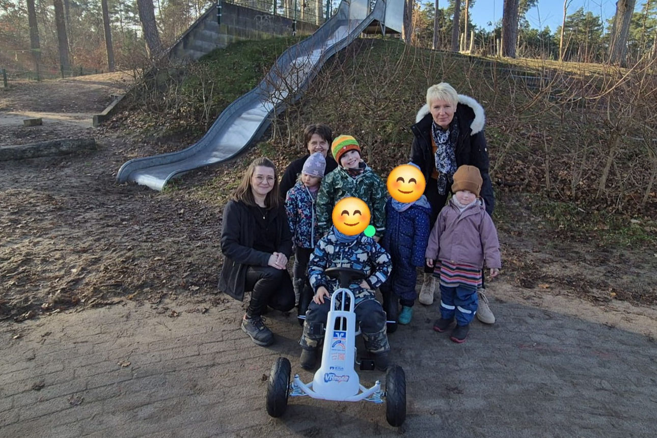 Erzieherinnen und Kita-Kinder im Kita-Garten mit Gokart.