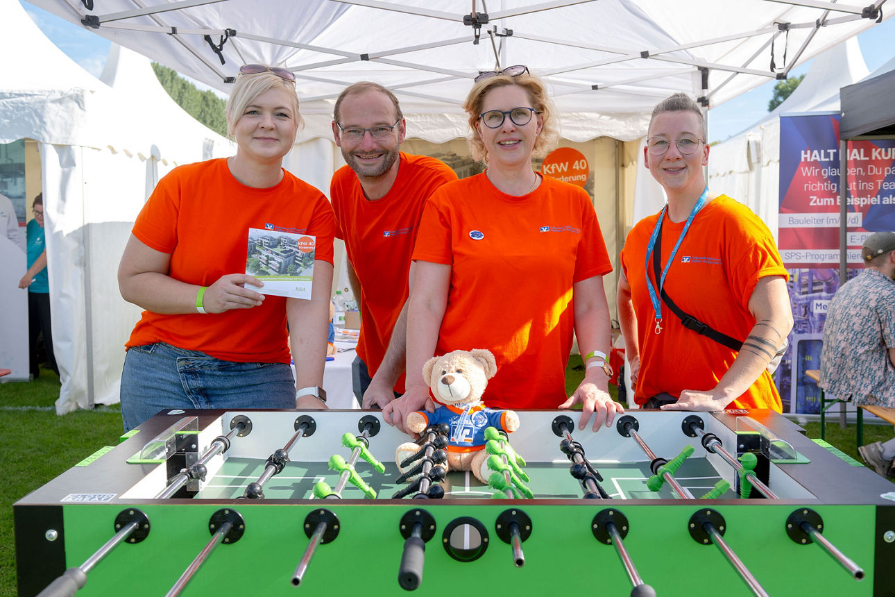 Vier Personen mit orangefrabenen T-Shirts an einem Tischkicker