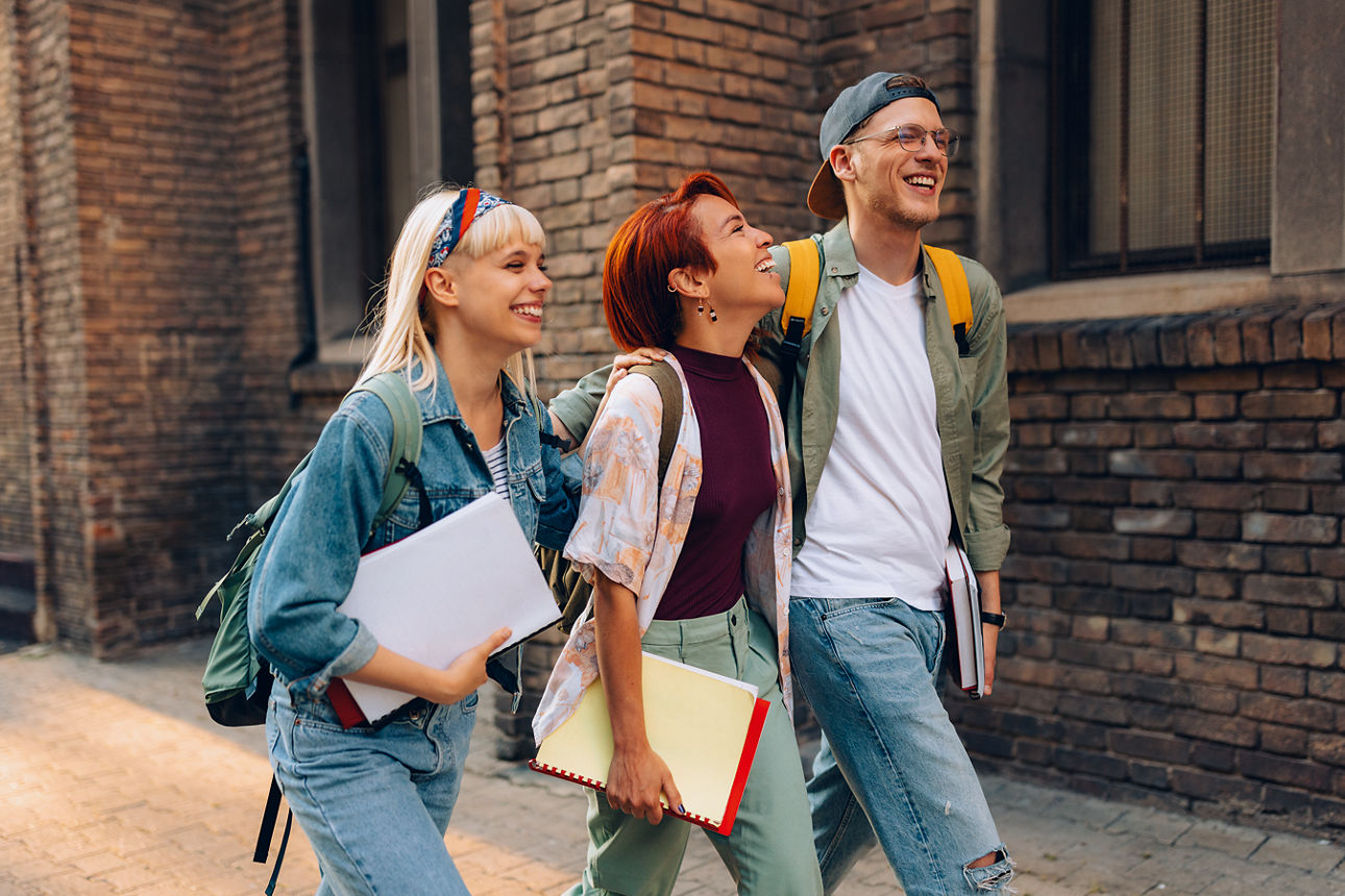 Gruppe fröhlicher Freunde aus dem College, die beim Spazierengehen auf der Straße Spaß haben