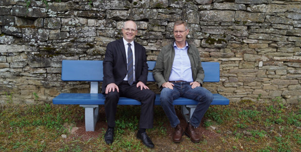 \Zwei Männer sitzen auf einer blauen Bank vor einer Steinmauer.