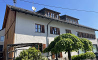 Zweistöckiges Haus mit Dachgauben und Bäumen im Vorgarten.