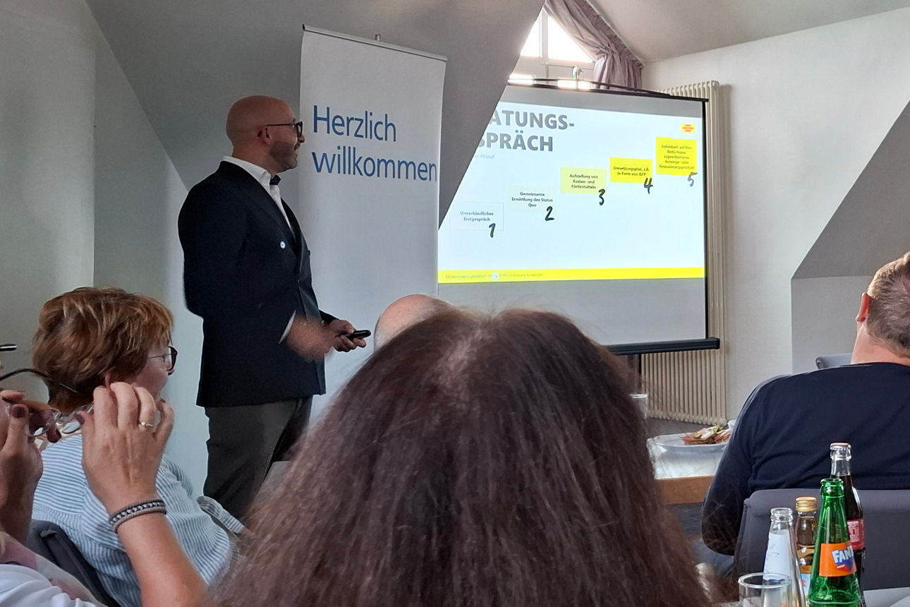 Ein professioneller Redner hält vor Publikum in einem hellen Konferenzraum einen Business-Workshop ab.