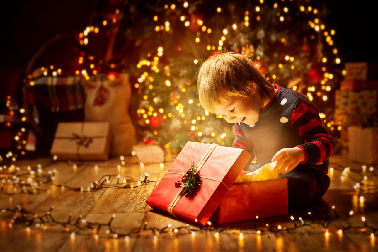 Kind öffnet Geschenk, glücklicher kleiner Junge schaut auf magisches Licht in der Schachtel, Kind sitzt vor dem Wei