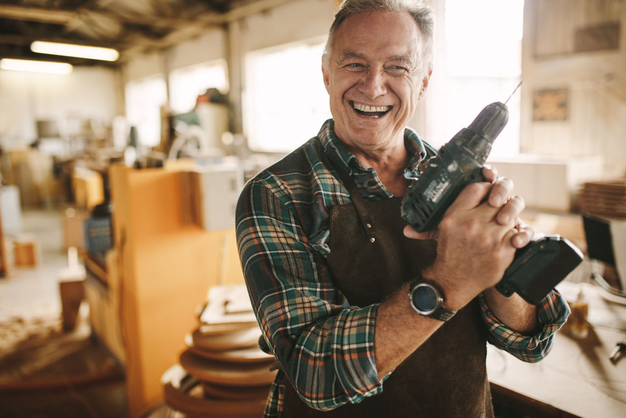 Handwerker steht in der Werkstatt und hat eine Bohrmaschine in der Hand.