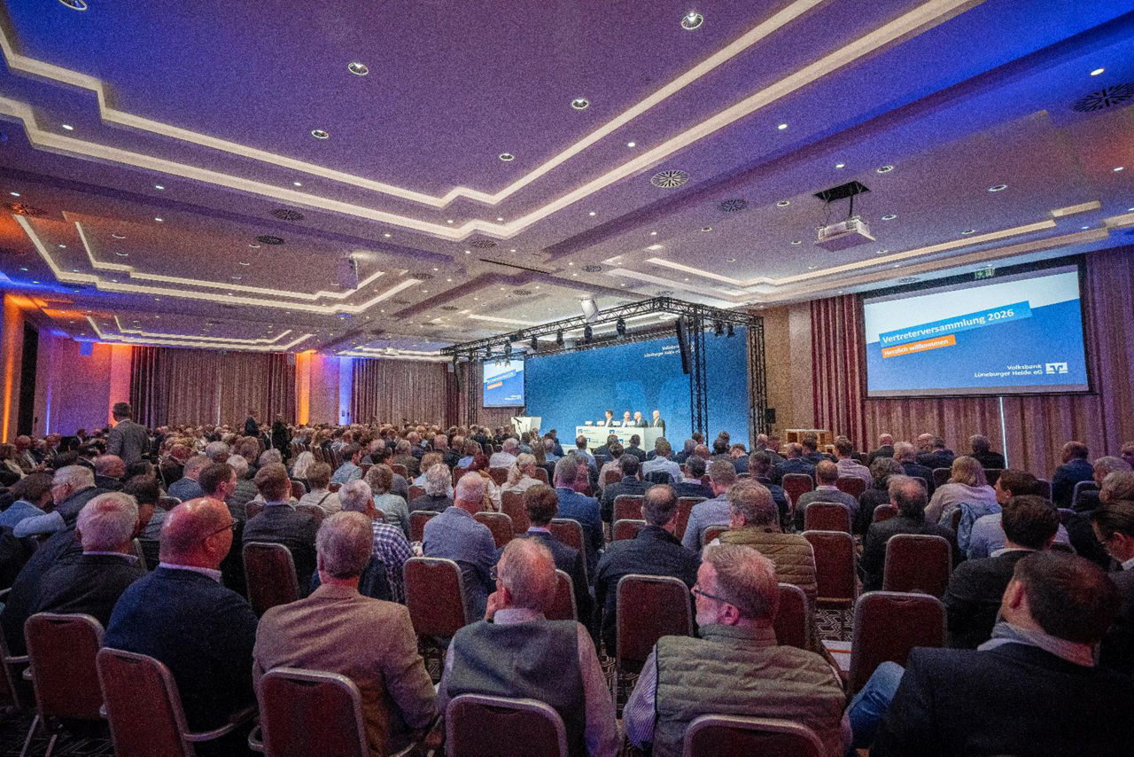 Blick in den illuminierten Saal mit Leinwänden, die die Präsentation zeigen und Blick auf die Bühne