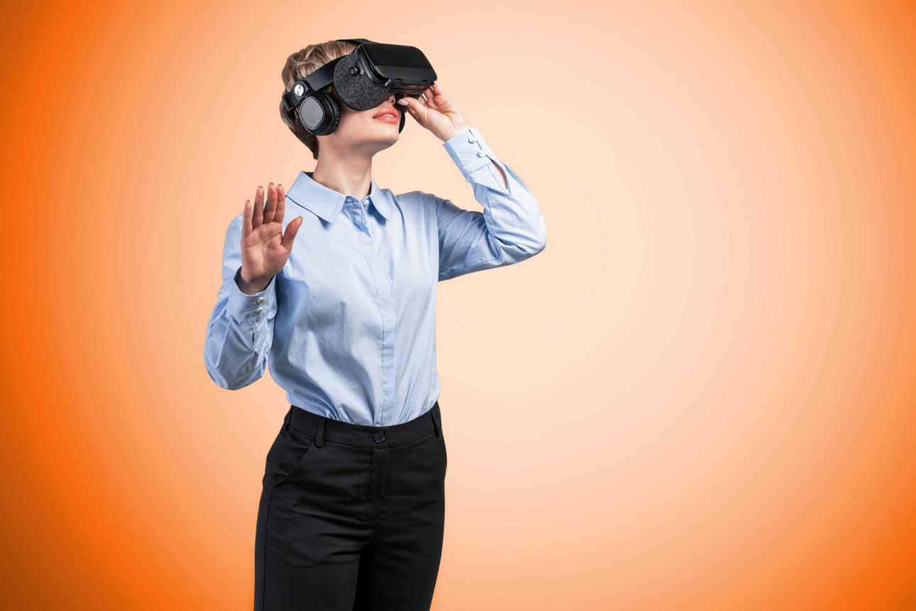 Ein Frau mit aufgesetzter VR Brille steht vor einem orangenem Hintergrund