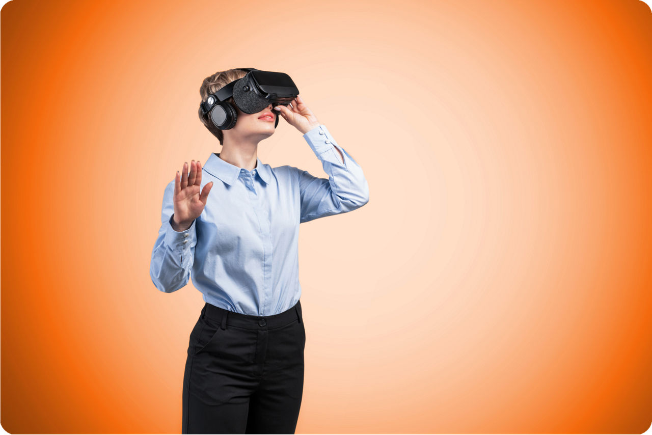 Ein Frau mit aufgesetzter VR Brille steht vor einem orangenem Hintergrund