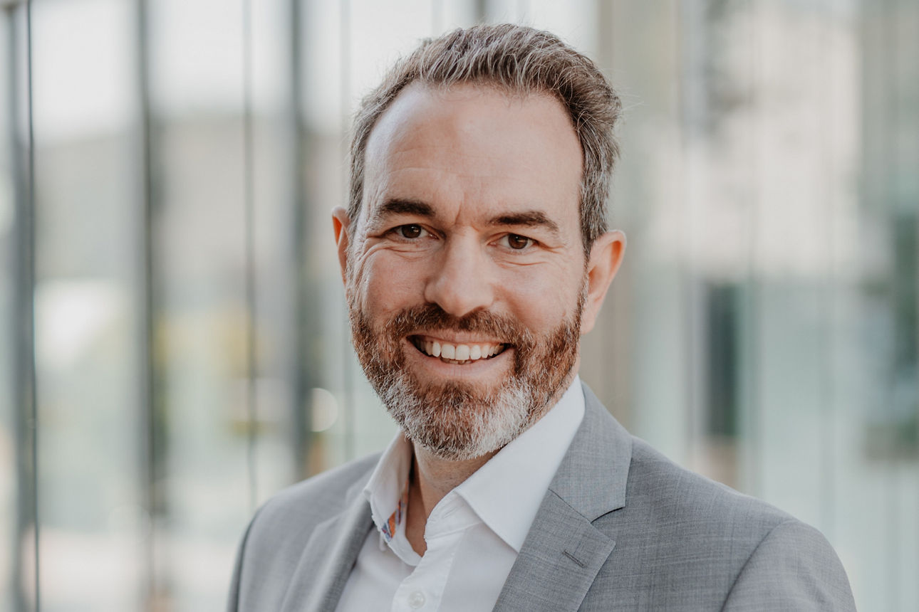 Porträt eines Mannes im grauen Anzug vor moderner Glasfassade, freundliche Businessaufnahme