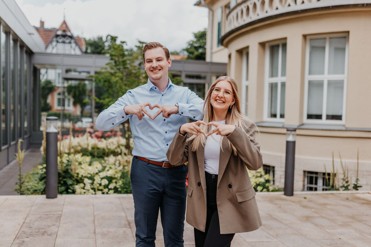 Zwei Bankmitarbeiter stehen nebeneinander und Formen ihre Hände zu einem Herz