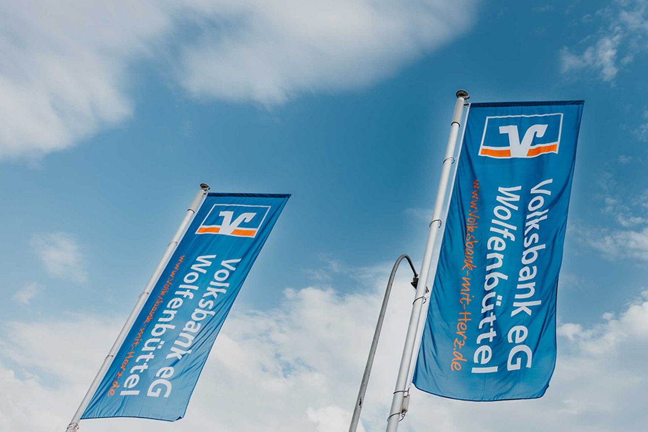 Fahnen der Volksbank eG Wolfenbüttel, im Hintergrund der blaue leicht bewölkte Himmel