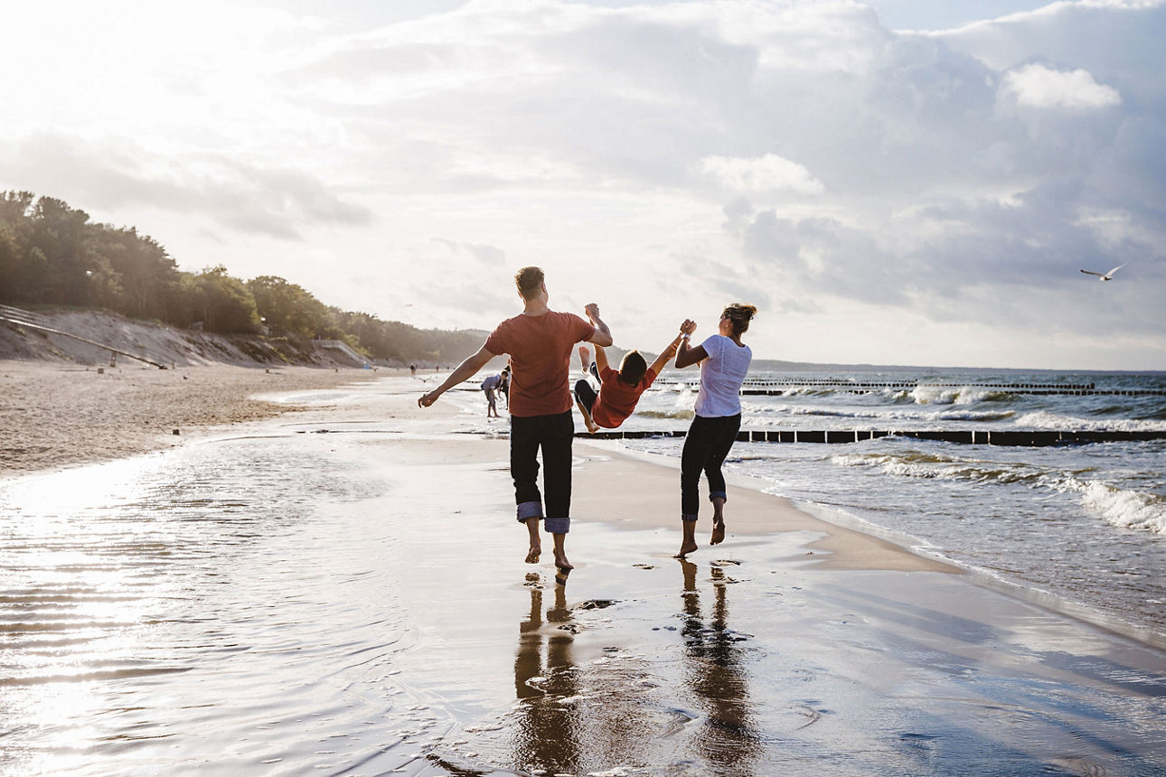 Eine Familie läuft Hand in Hand am Strand entlang, während die Wellen sanft ans Ufer schlagen.