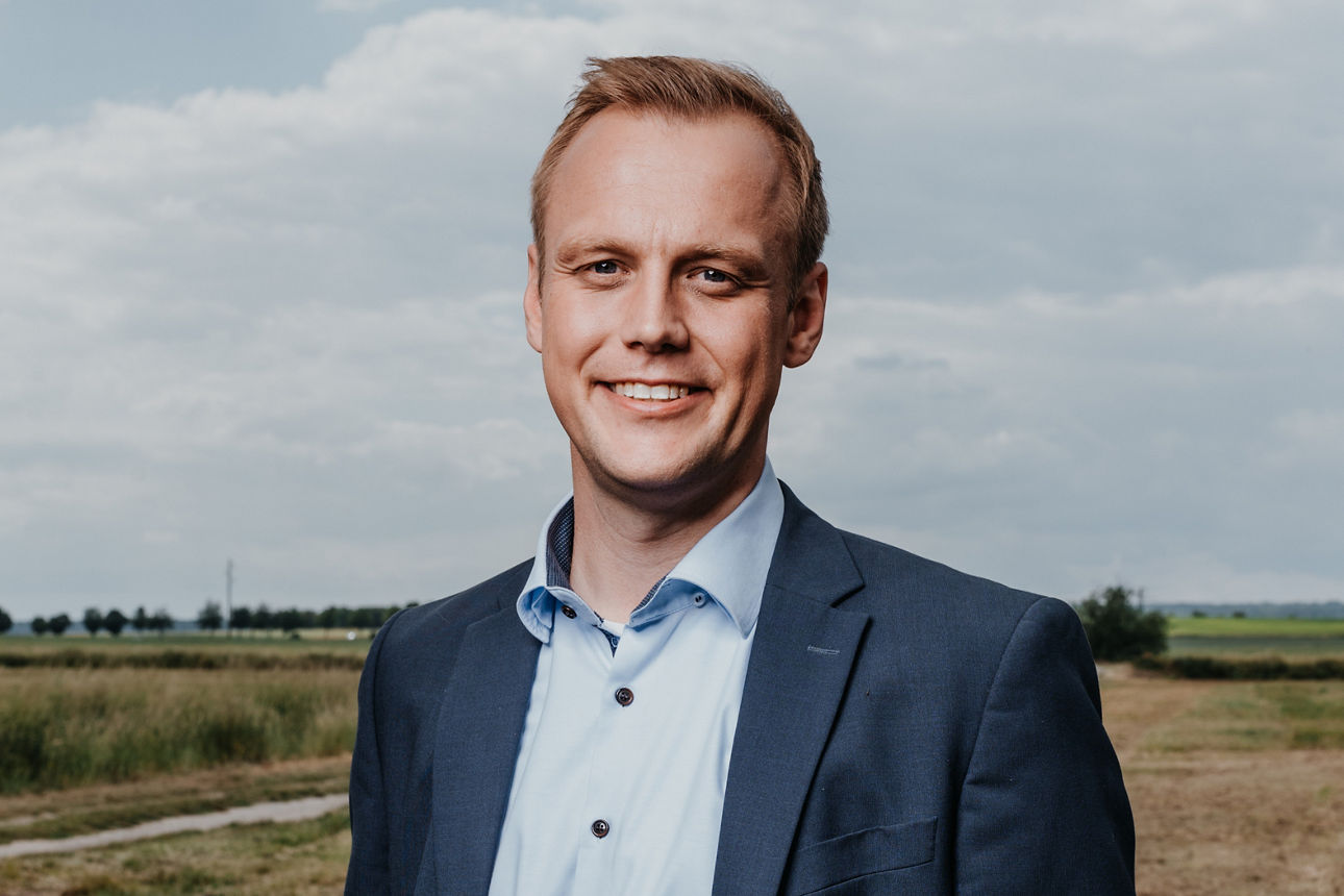 Berater Meier steht in Business Kleidung auf einem Feld.