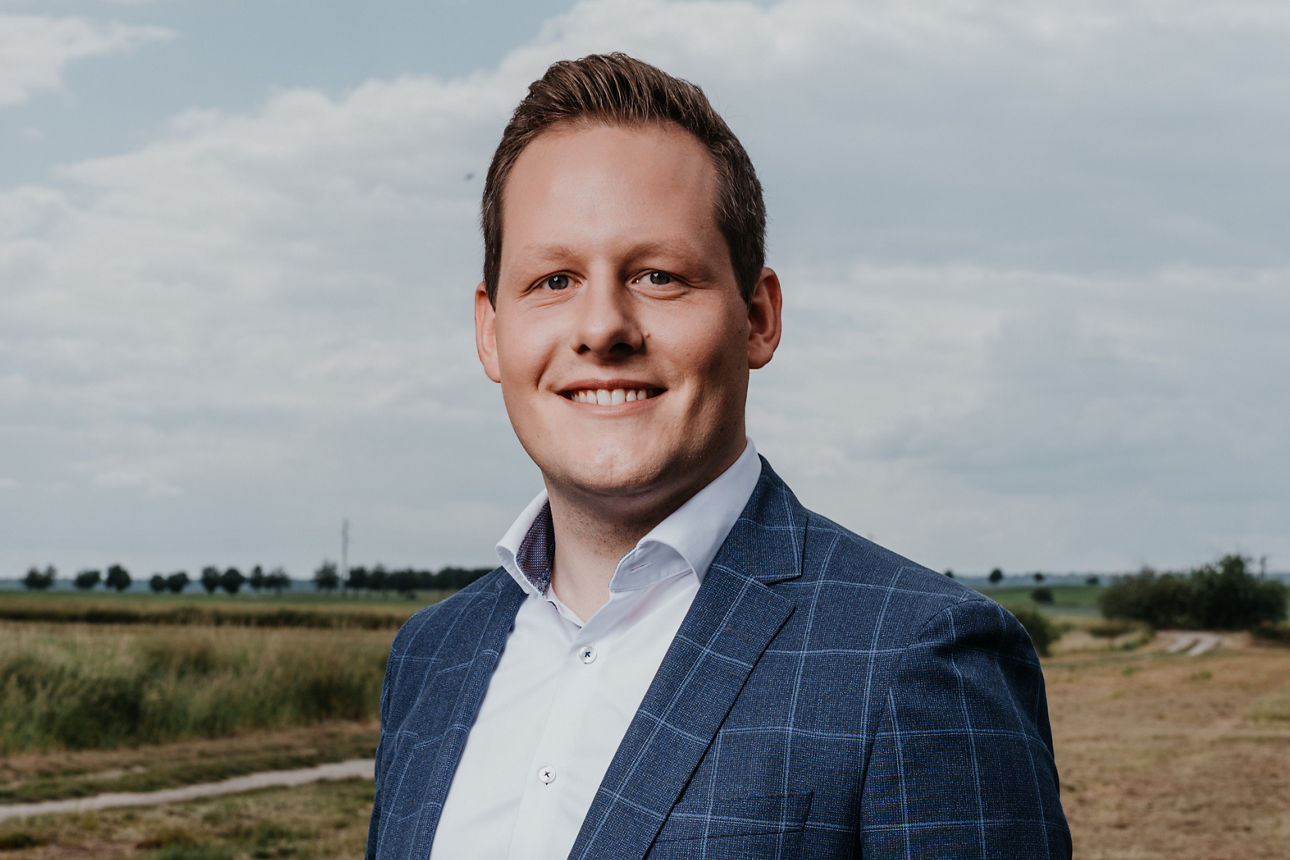 Berater Scholz steht in Business Kleidung auf einem Feld.