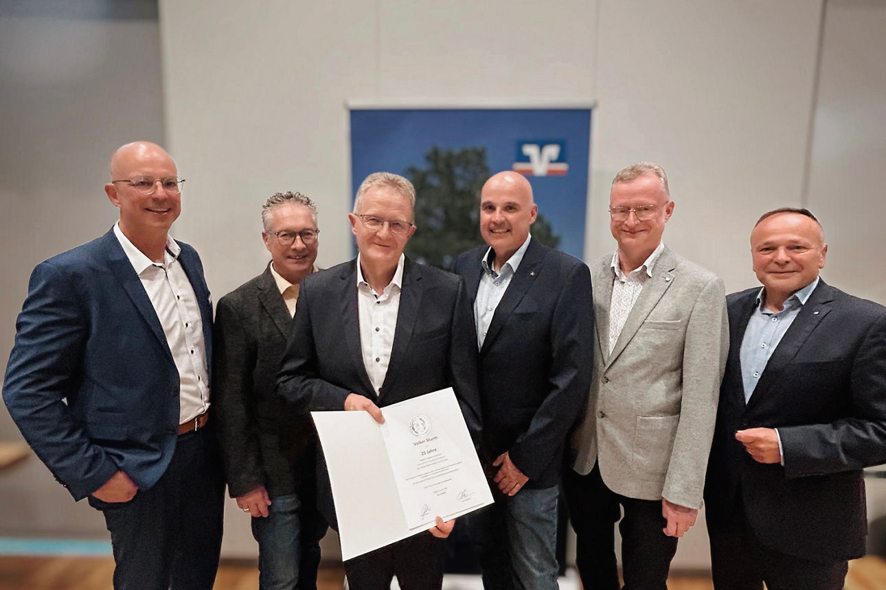 Ein Mann, der ein Zertifikat in der Hand hält, steht während einer Fachveranstaltung inmitten einer Gruppe von fünf Kollegen.