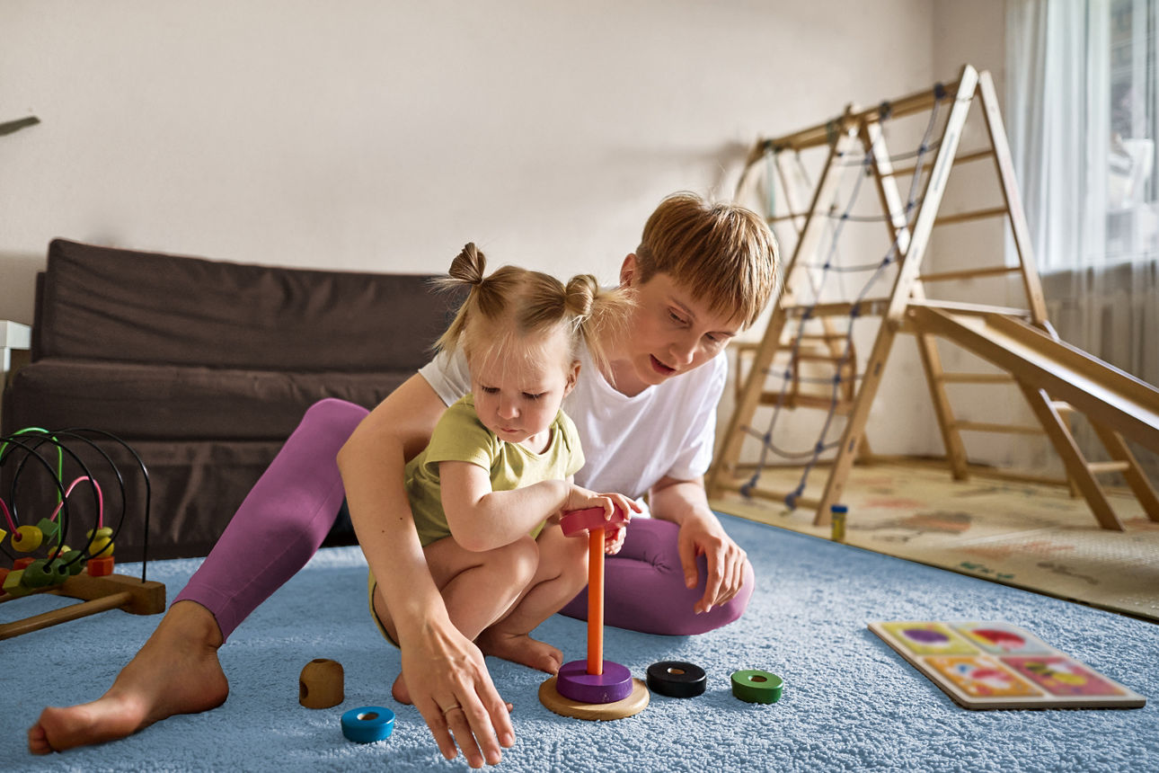 Mutter mit Kind spielen zusammen auf dem Teppich ein Holzspiel