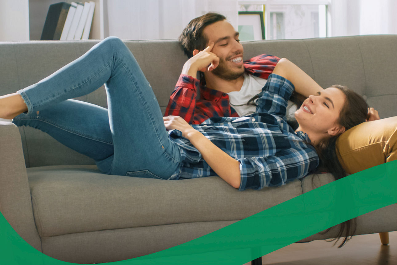 Ein Paar liegt auf dem Sofa und lächelt sich an.