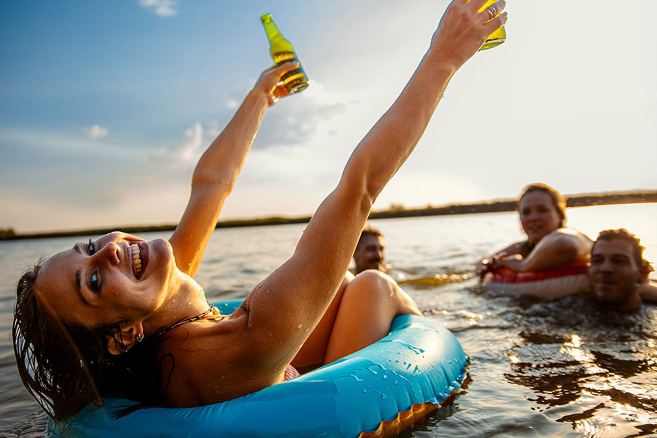 Eine junge Frau sitzt in einem Reifen und treibt damit auf dem Wasser. Sie strahlt freudig in die Kamera.