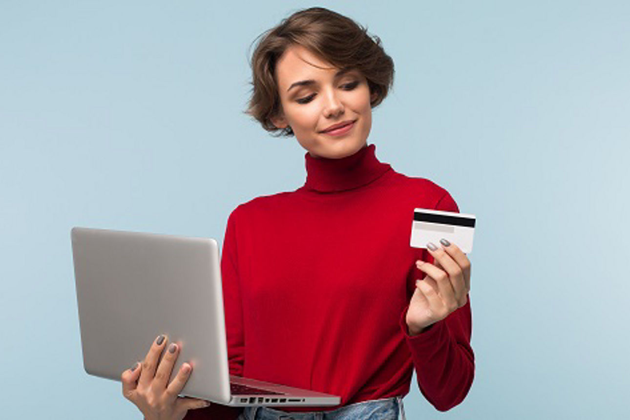 Junge Frau in rotem Rollkragenpullover hält Laptop in einer Hand und Kreditkarte in der anderen.