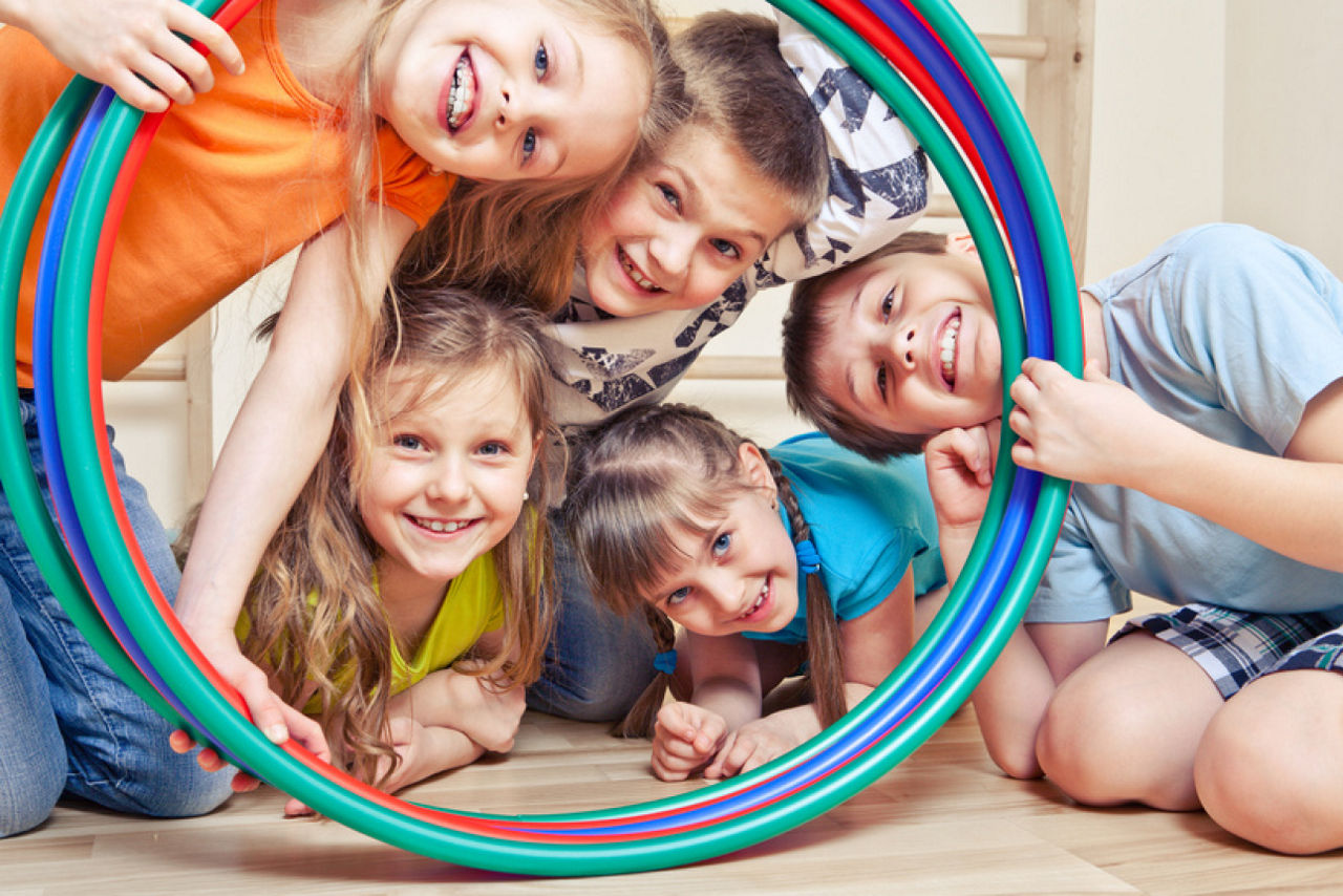Mehrere Kinder liegen auf dem Boden und schauen durch bunte Hula-Hoop-Reifen.