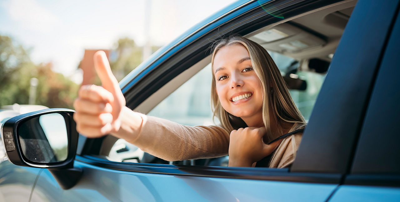 Junge Frau zeigt Daumen hoch aus einem Auto