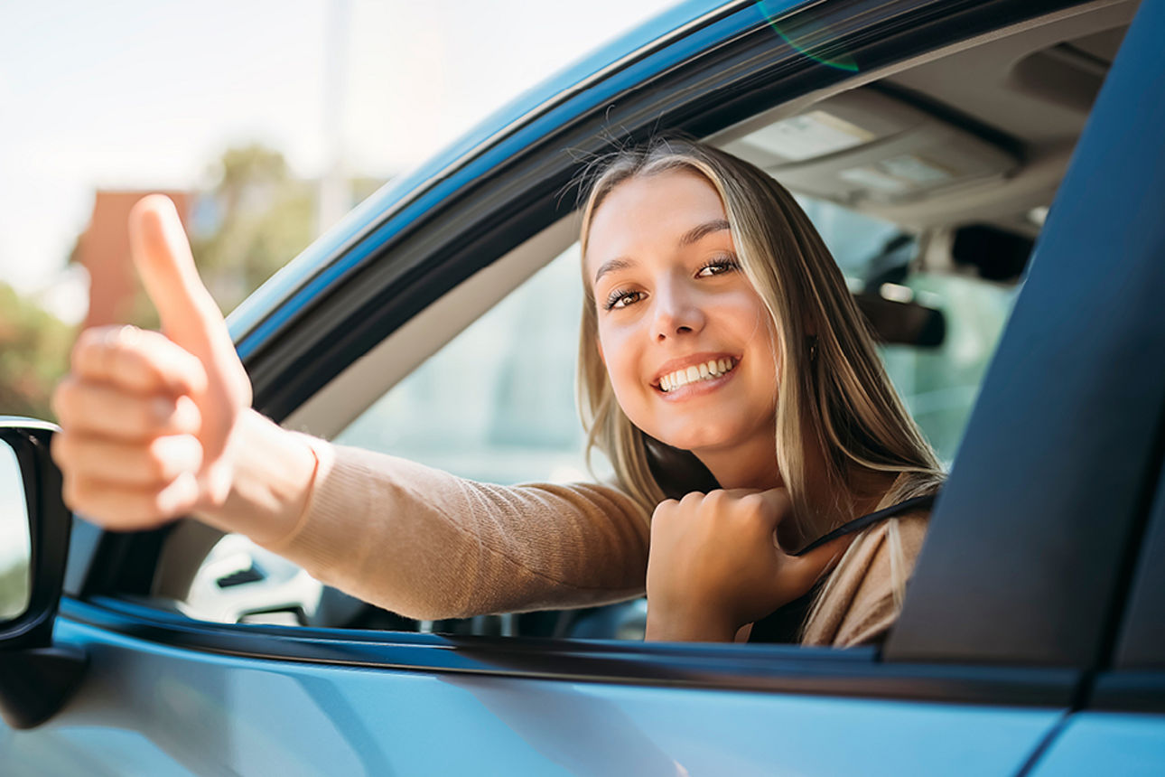 Junge Frau zeigt Daumen hoch aus einem Auto