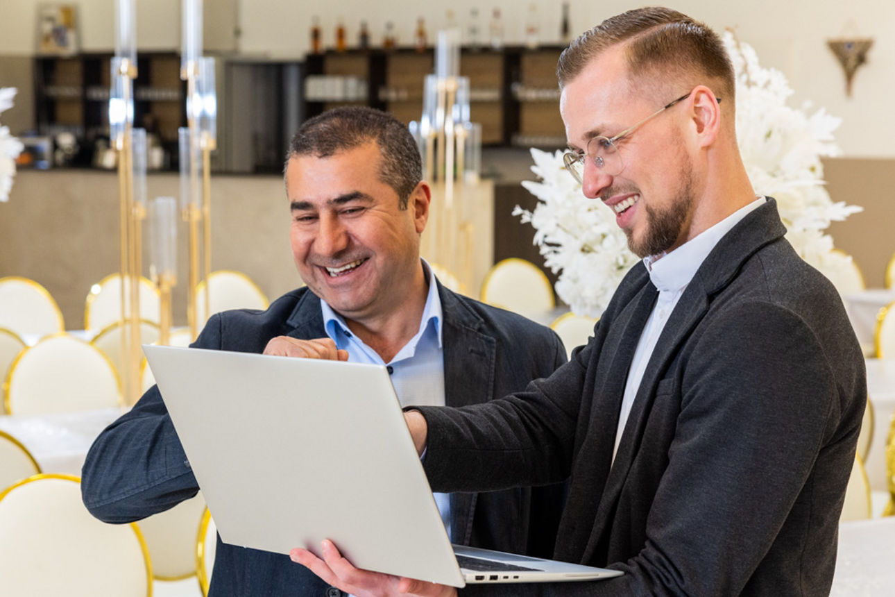 Ein Geschäftsführer eines Unternehmens und ein Bankberater schauen auf einen Laptop