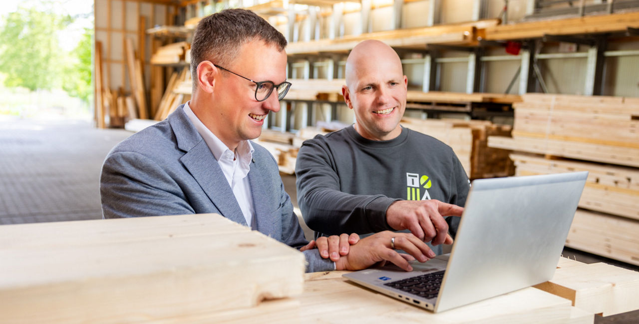 Ein Geschäftsführer eines Unternehmens und ein Bankberater schauen auf einen Laptop