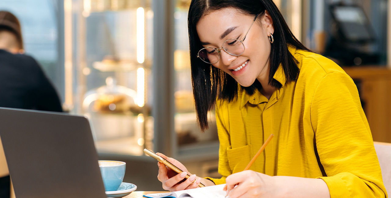 Junge Frau mit Handy und Bleistift vor Laptop und Notizblock