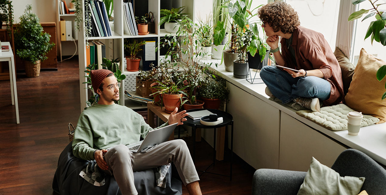 Mann im Sitzsack mit Laptop und Frau mit Tablet auf Fensterbank sitzend